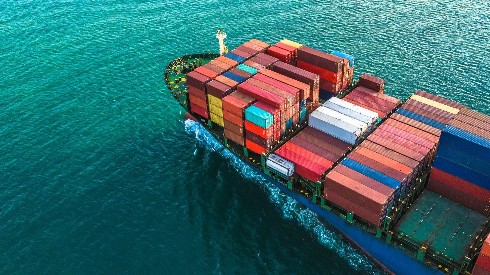 Aerial view of a loaded container ship cutting through turquoise water