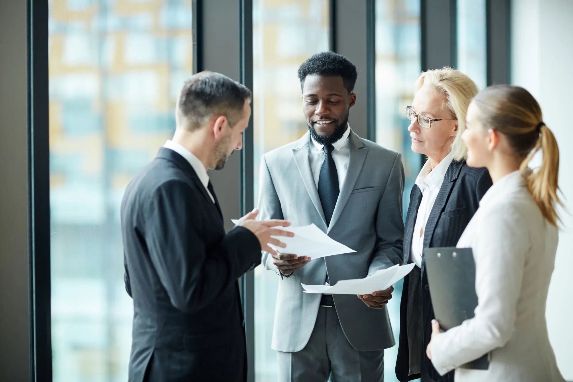 Two brokers at an office window reviewing documents together