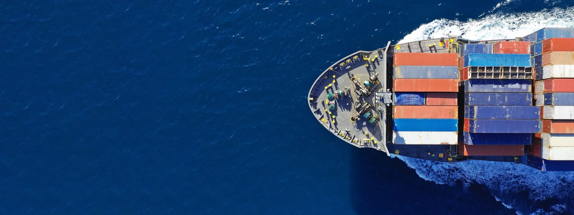 An aerial view of a container ship cutting diagonally through deep blue water