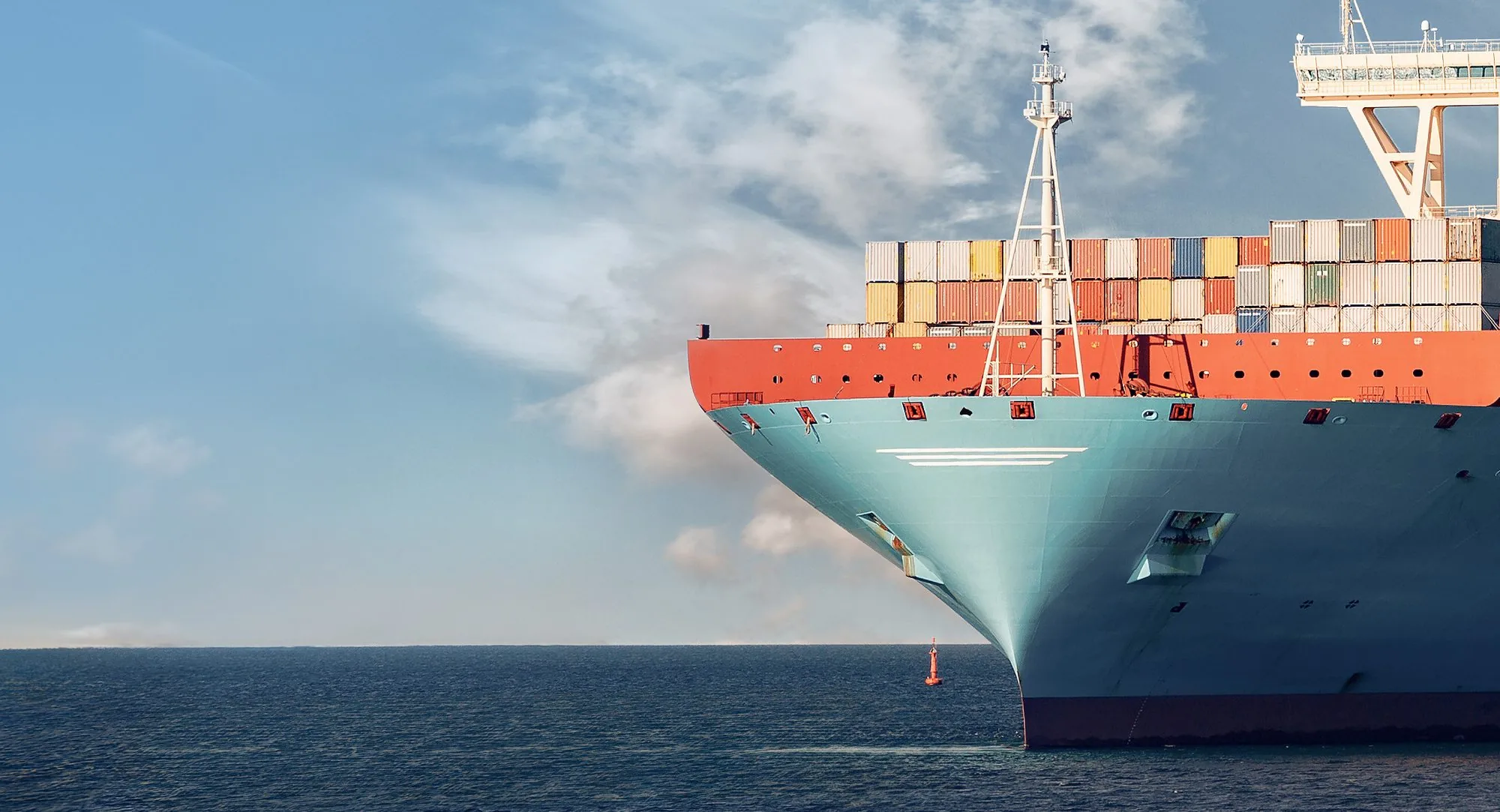 A loaded container ship pushing through calm open sea, seen from the bow