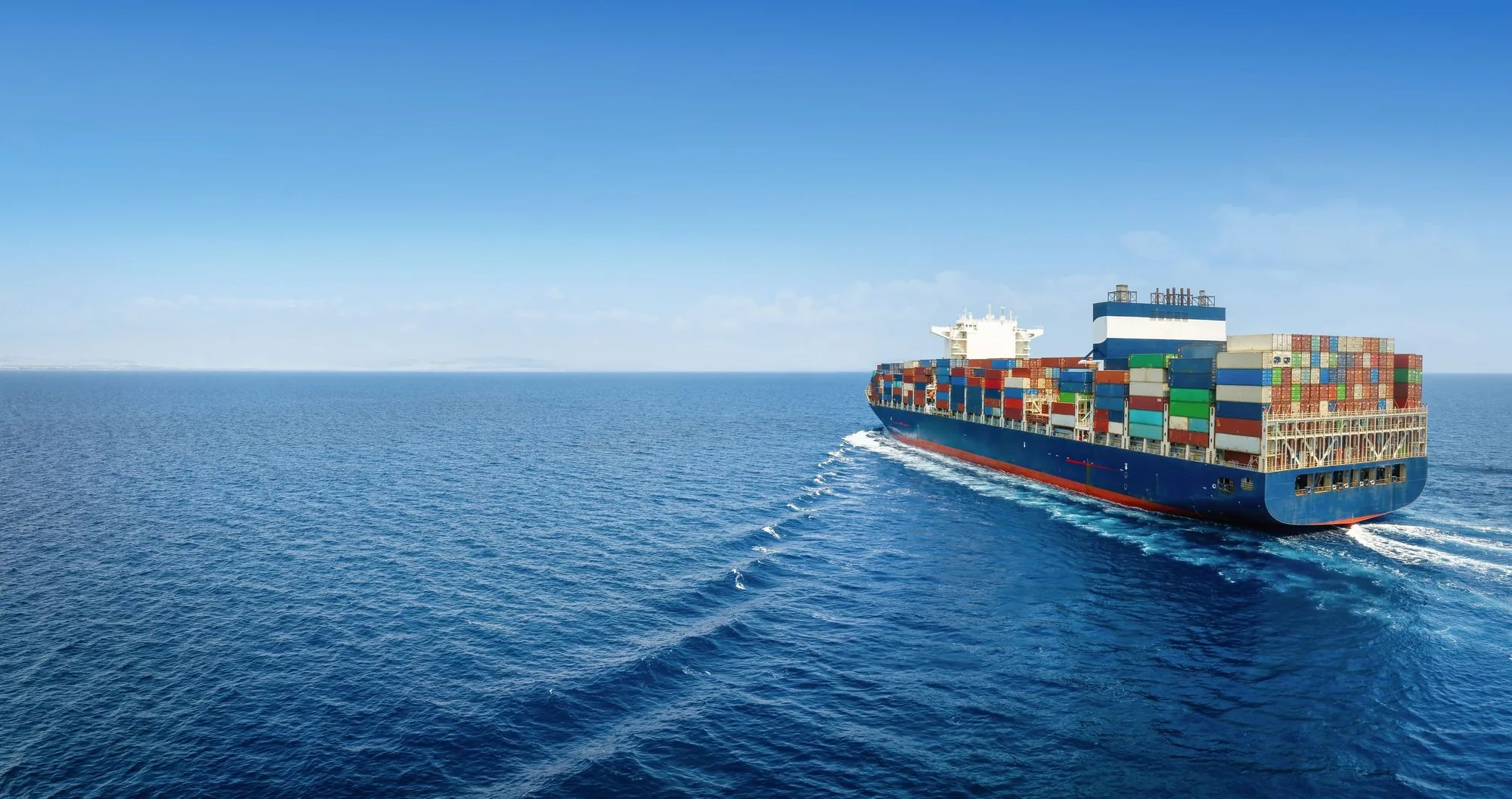 A loaded container ship crossing a flat blue ocean